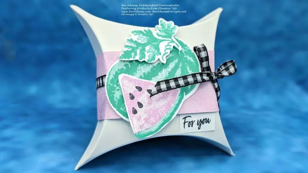A square pillow box decorated with a light purple band and a black and white plaid ribbon. There is a stamped image of a watermelon and also a slice of watermelon.